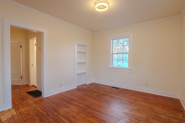 empty room featuring hardwood / wood-style flooring, ornamental molding, and built in shelves