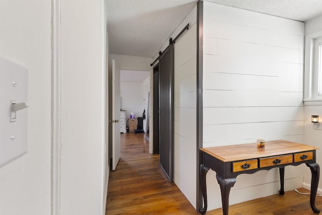 corridor with dark hardwood / wood-style flooring, a barn door, and a textured ceiling