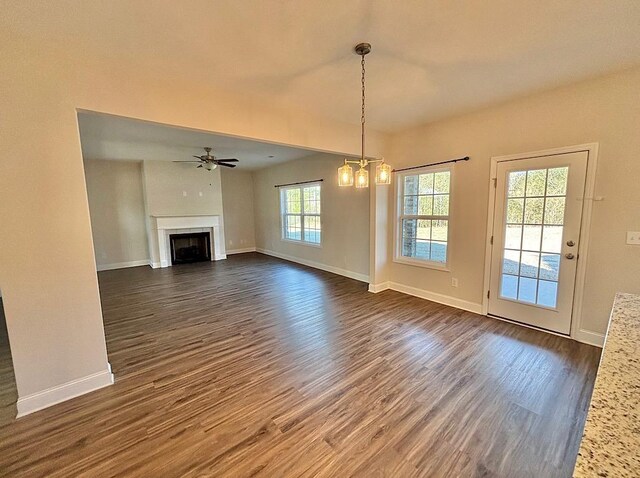 unfurnished living room featuring ceiling fan with notable chandelier and dark wood-type flooring