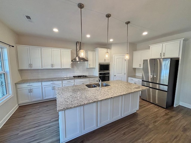 kitchen with appliances with stainless steel finishes, pendant lighting, sink, white cabinetry, and wall chimney range hood