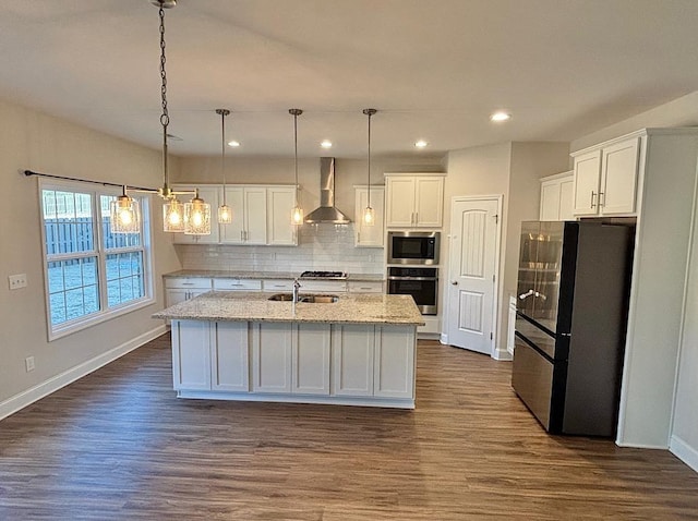 kitchen featuring wall chimney exhaust hood, white cabinets, a center island with sink, and appliances with stainless steel finishes