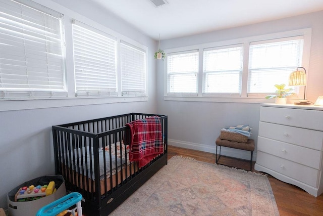 bedroom with multiple windows, light hardwood / wood-style flooring, and a nursery area