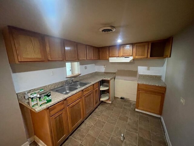  - kitchen featuring under cabinet range hood, brown cabinets, light countertops, and dark tile patterned flooring