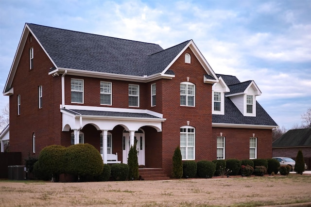 view of front of home featuring a porch, brick siding, central AC, and roof with shingles