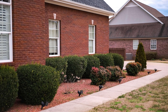 view of side of property featuring a shingled roof, brick siding, and fence