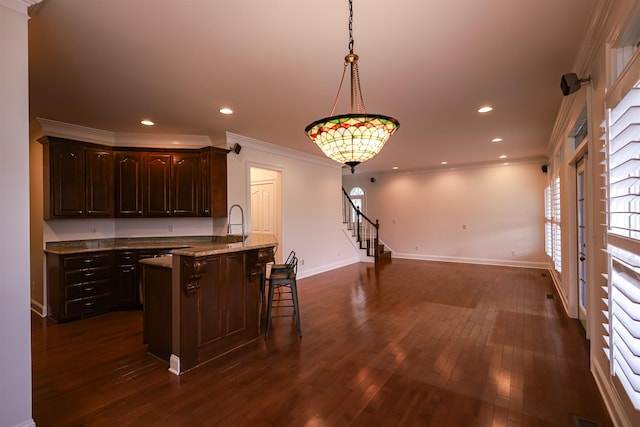 kitchen with light stone counters, crown molding, hanging light fixtures, dark brown cabinets, and a kitchen bar