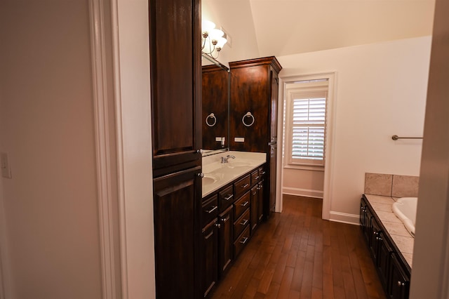 full bath featuring a sink, wood finished floors, baseboards, double vanity, and a bathtub