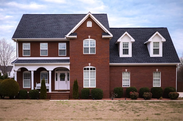 view of front of house featuring covered porch, a shingled roof, and brick siding