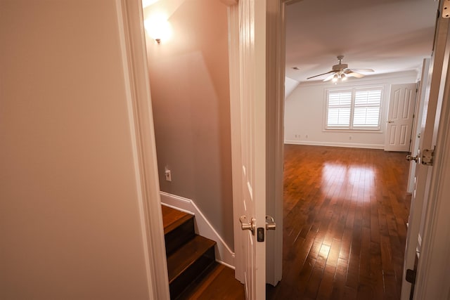 corridor featuring dark wood-type flooring, vaulted ceiling, baseboards, and stairs