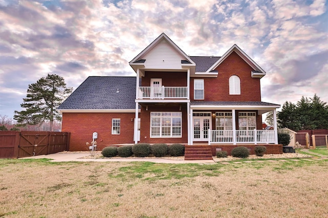 back of property at dusk with a porch, a fenced backyard, brick siding, a yard, and a gate