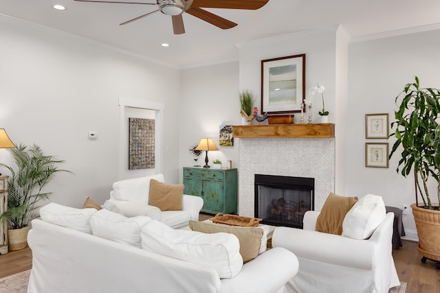 living room featuring crown molding, ceiling fan, a fireplace, and light hardwood / wood-style floors