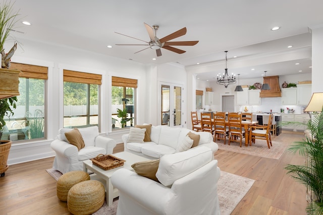 living room with crown molding, ceiling fan with notable chandelier, and light hardwood / wood-style flooring