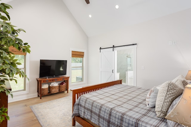 bedroom featuring a barn door, high vaulted ceiling, and light wood-type flooring