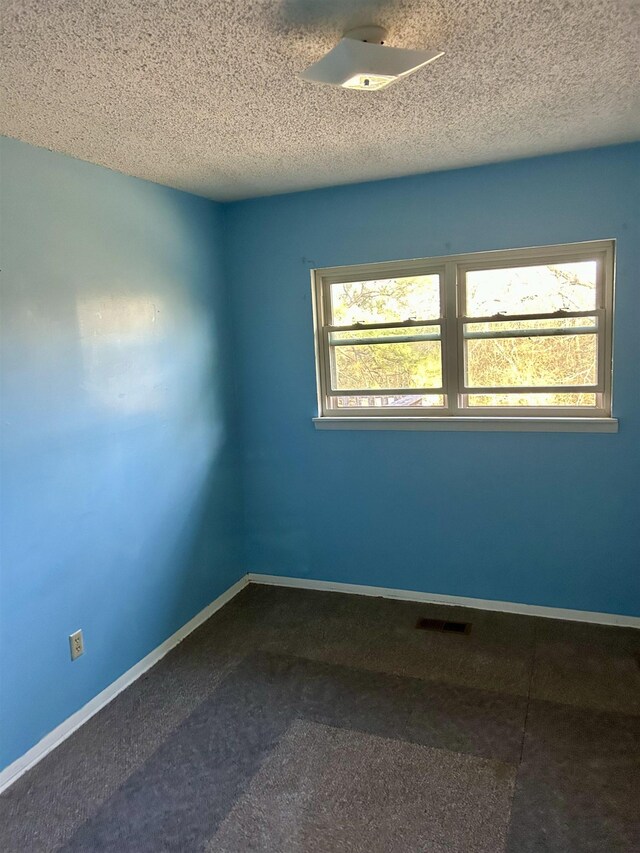 empty room featuring visible vents, a textured ceiling, and baseboards