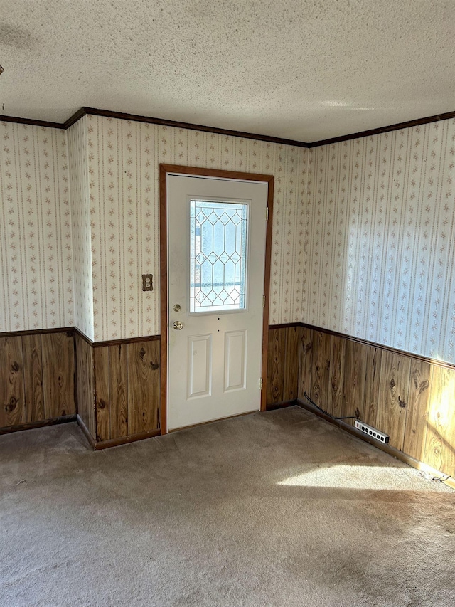 entrance foyer featuring wainscoting, a textured ceiling, wallpapered walls, and ornamental molding