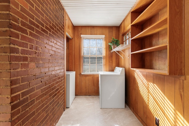 washroom featuring washing machine and dryer, brick wall, light tile patterned floors, and wood walls