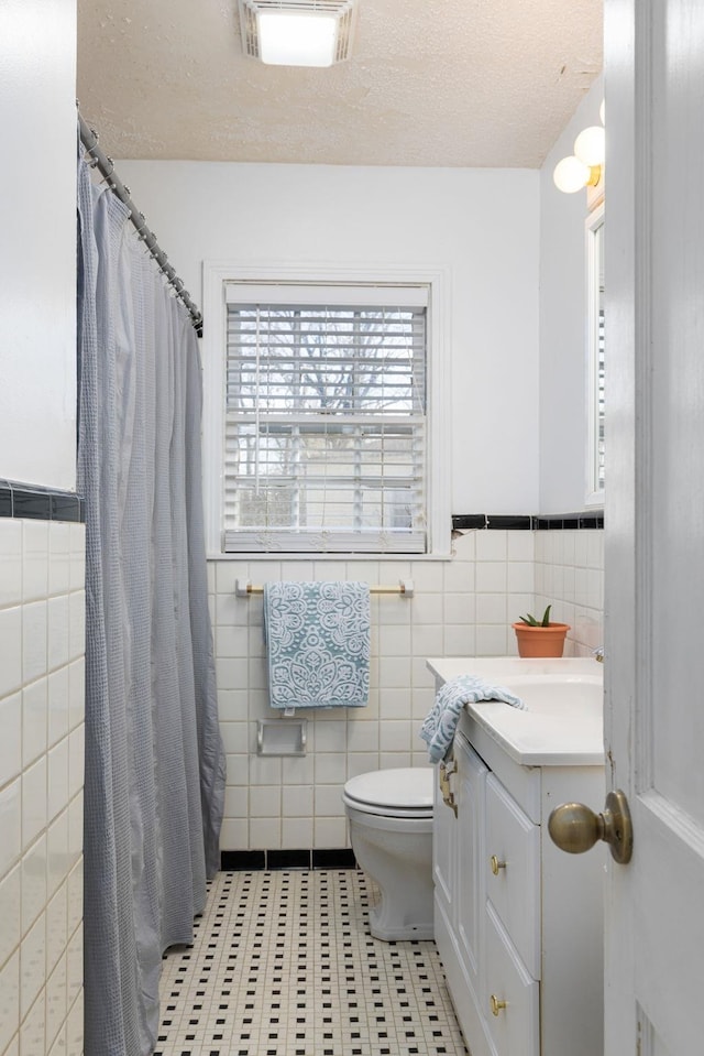 bathroom featuring vanity, toilet, tile walls, and a textured ceiling