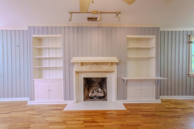 unfurnished living room featuring built in features, light hardwood / wood-style flooring, crown molding, and wood walls