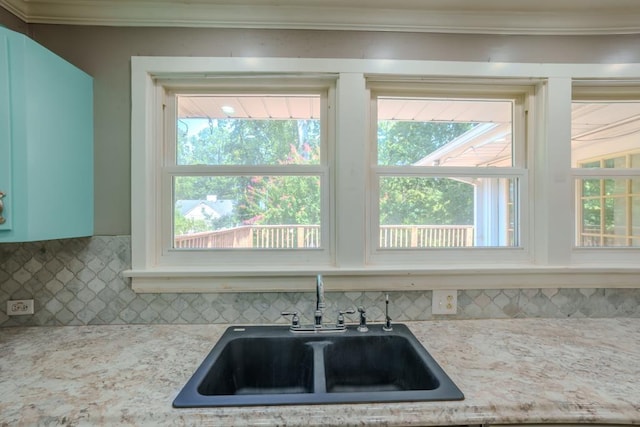 kitchen with light stone countertops, backsplash, crown molding, and sink