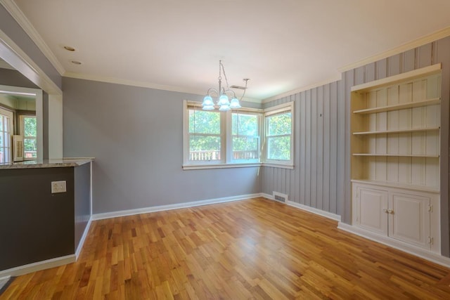 unfurnished dining area featuring built in shelves, light hardwood / wood-style flooring, crown molding, and an inviting chandelier