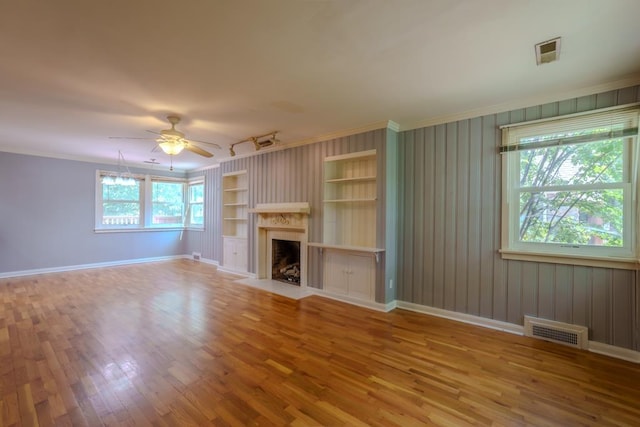 unfurnished living room featuring ceiling fan, built in features, hardwood / wood-style flooring, and ornamental molding