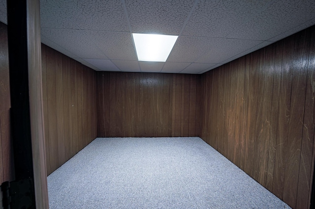 carpeted spare room featuring a paneled ceiling and wood walls