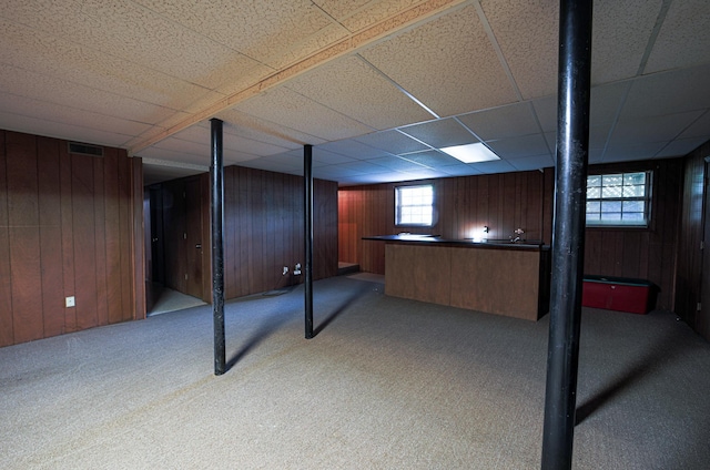 basement featuring carpet, a drop ceiling, wooden walls, and pool table