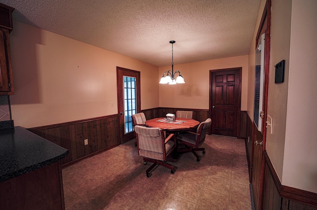 dining room with wood walls, a chandelier, and a textured ceiling