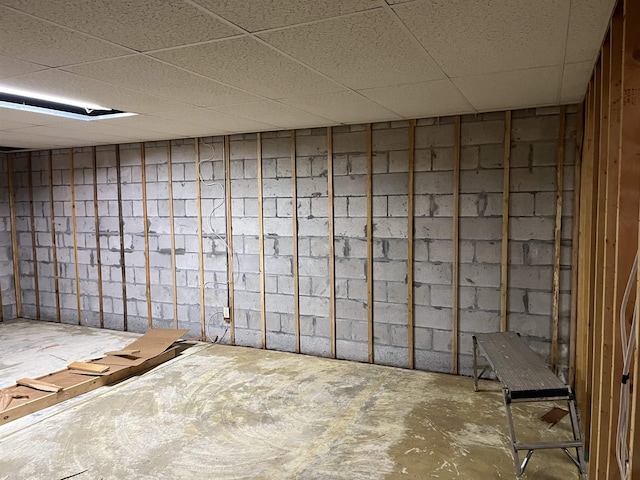 unfinished basement featuring a paneled ceiling and concrete block wall