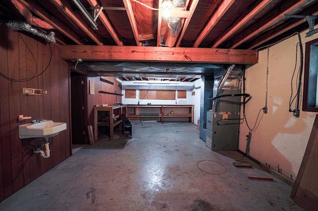 basement with heating unit, wood walls, and sink