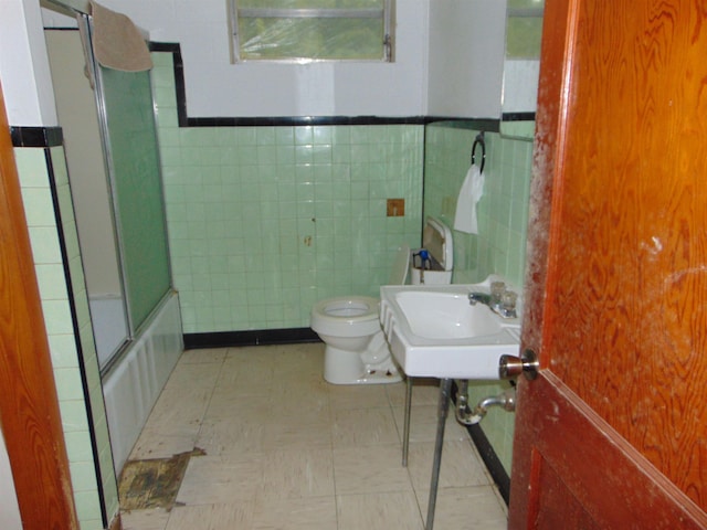 full bathroom featuring sink, combined bath / shower with glass door, tile walls, and toilet