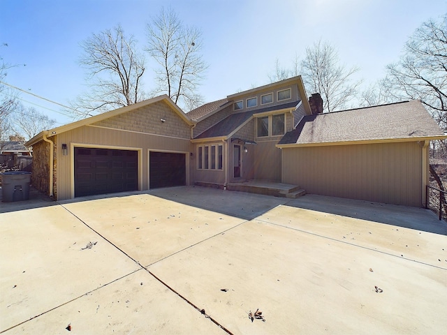 view of front facade featuring an attached garage, a chimney, concrete driveway, and roof with shingles