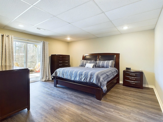 bedroom with visible vents, baseboards, a drop ceiling, and wood finished floors