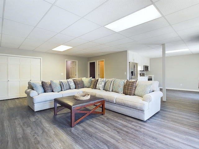 living area featuring dark wood-type flooring, a paneled ceiling, and baseboards