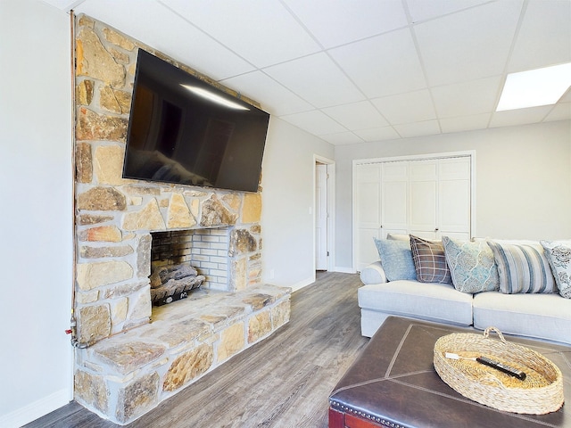 living area with a stone fireplace, a drop ceiling, wood finished floors, and baseboards