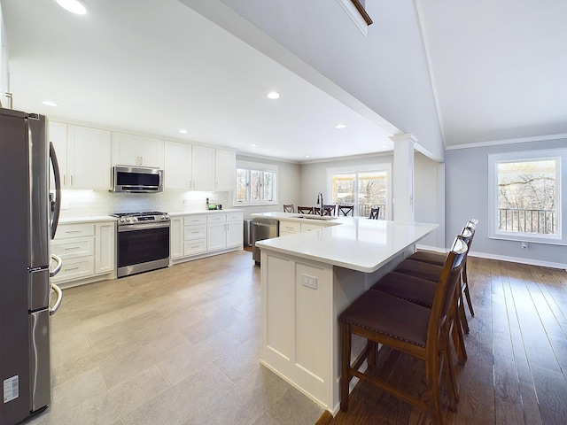 kitchen featuring tasteful backsplash, appliances with stainless steel finishes, ornamental molding, a sink, and ornate columns