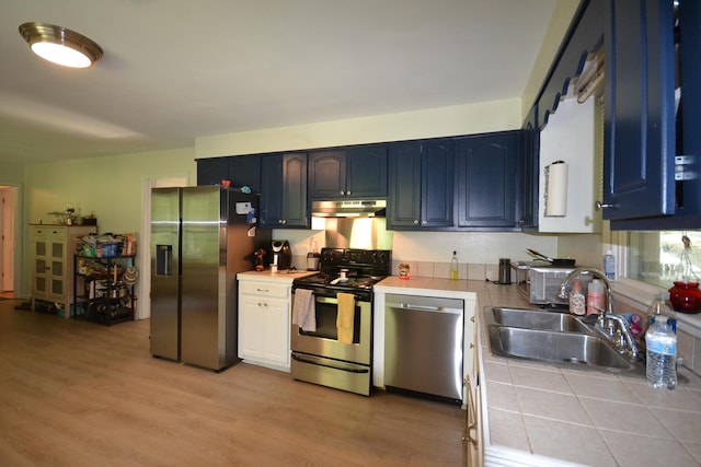 kitchen with tile countertops, sink, light wood-type flooring, blue cabinetry, and stainless steel appliances