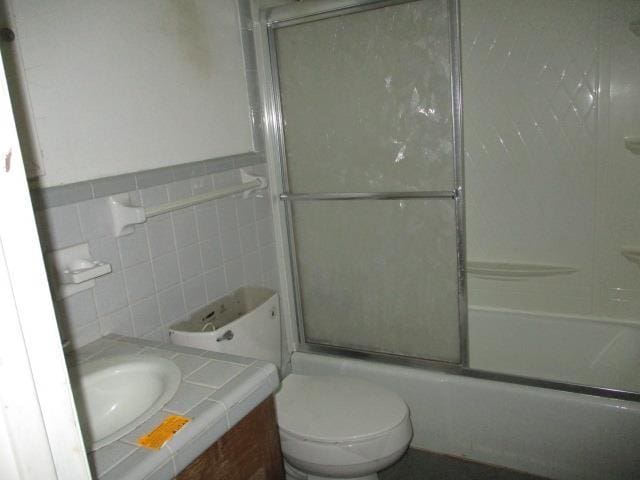 full bathroom featuring combined bath / shower with glass door, toilet, tile walls, and vanity