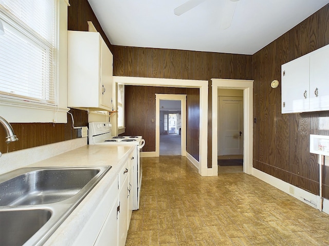 kitchen with white cabinetry, white range with electric cooktop, wooden walls, and sink