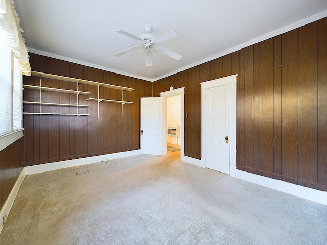 unfurnished bedroom with ceiling fan, wood walls, ornamental molding, and light carpet