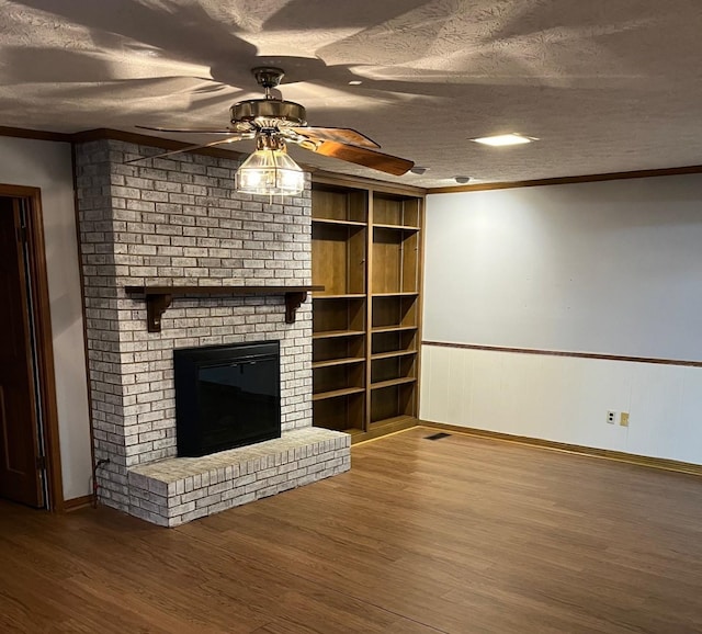 unfurnished living room with crown molding, a textured ceiling, built in features, ceiling fan, and a fireplace