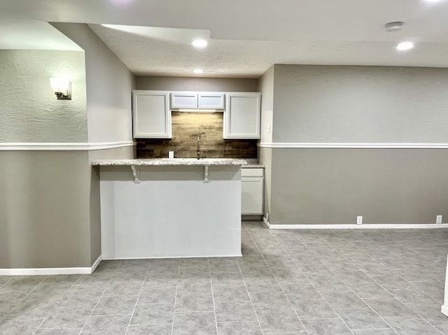  - kitchen featuring recessed lighting, decorative backsplash, light stone counters, a kitchen breakfast bar, and white cabinetry