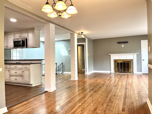  - unfurnished living room with wood finished floors, a chandelier, and a glass covered fireplace