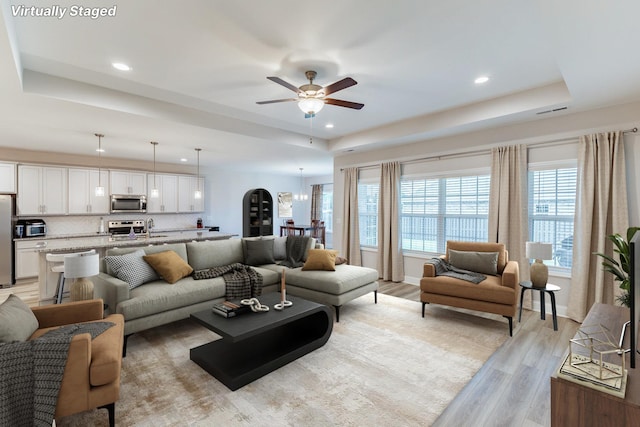 living area featuring light wood-type flooring, a tray ceiling, visible vents, and ceiling fan