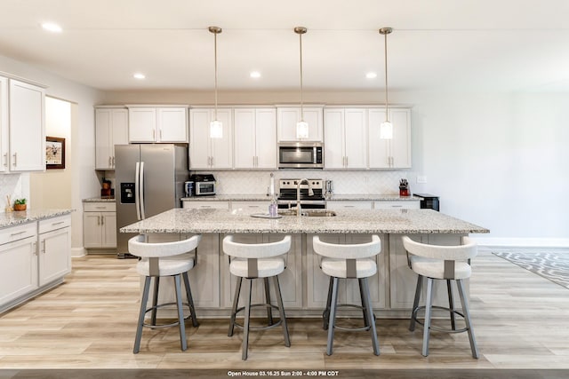 kitchen featuring decorative backsplash, light wood-style flooring, stainless steel appliances, and an island with sink