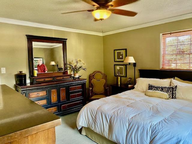 bedroom featuring carpet flooring, a textured ceiling, ceiling fan, and ornamental molding