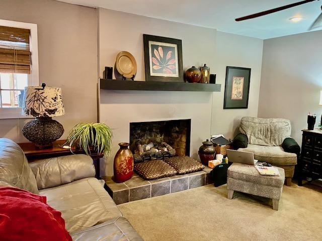 sitting room with carpet, ceiling fan, and a tiled fireplace