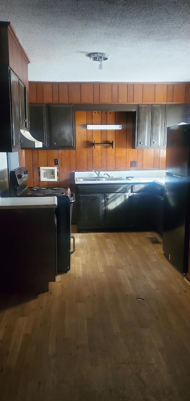 kitchen with black fridge, a textured ceiling, electric range, and light wood-type flooring