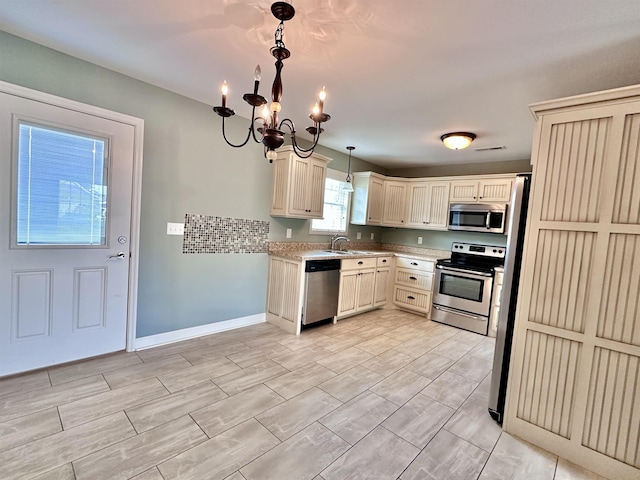  - kitchen featuring stainless steel appliances, a sink, a chandelier, cream cabinets, and decorative light fixtures