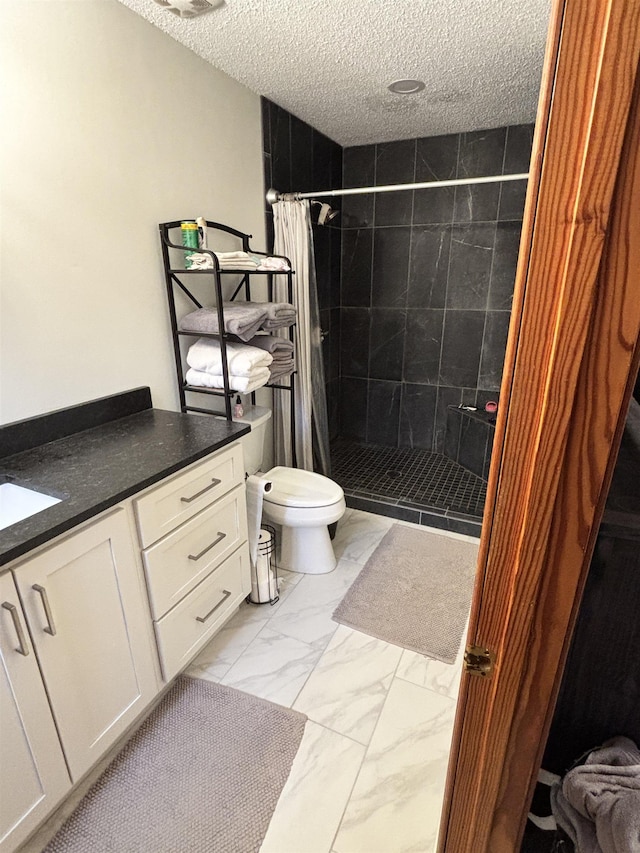 full bath with a textured ceiling, toilet, vanity, marble finish floor, and a tile shower